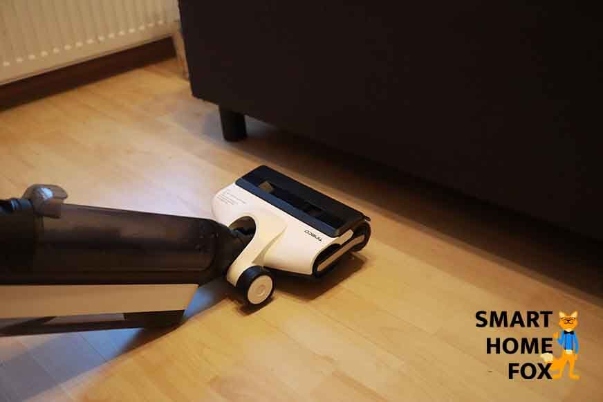 Man sieht, wie der Bereich unter einem Sofa mit dem Tineco Floor One S5 Combo gereinigt wird.